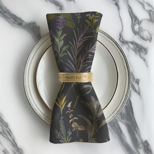 Set of four dark charcoal cloth napkins with a repeating pattern of muted purple, green, and gold herbs and flowers in an elegant botanical design.